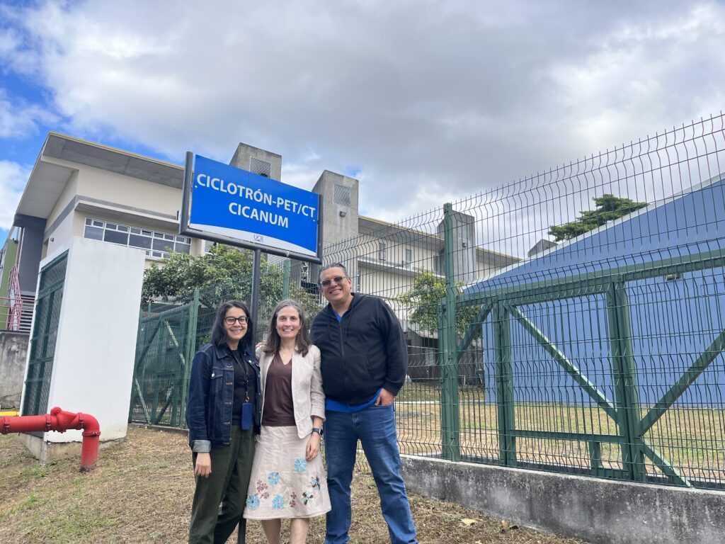 Three people stand outside a cyclotron facility in Costa Rica